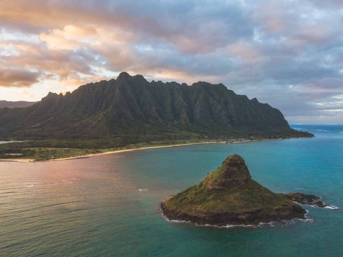 drone shot image of an island in the ocean in front of a mountain range