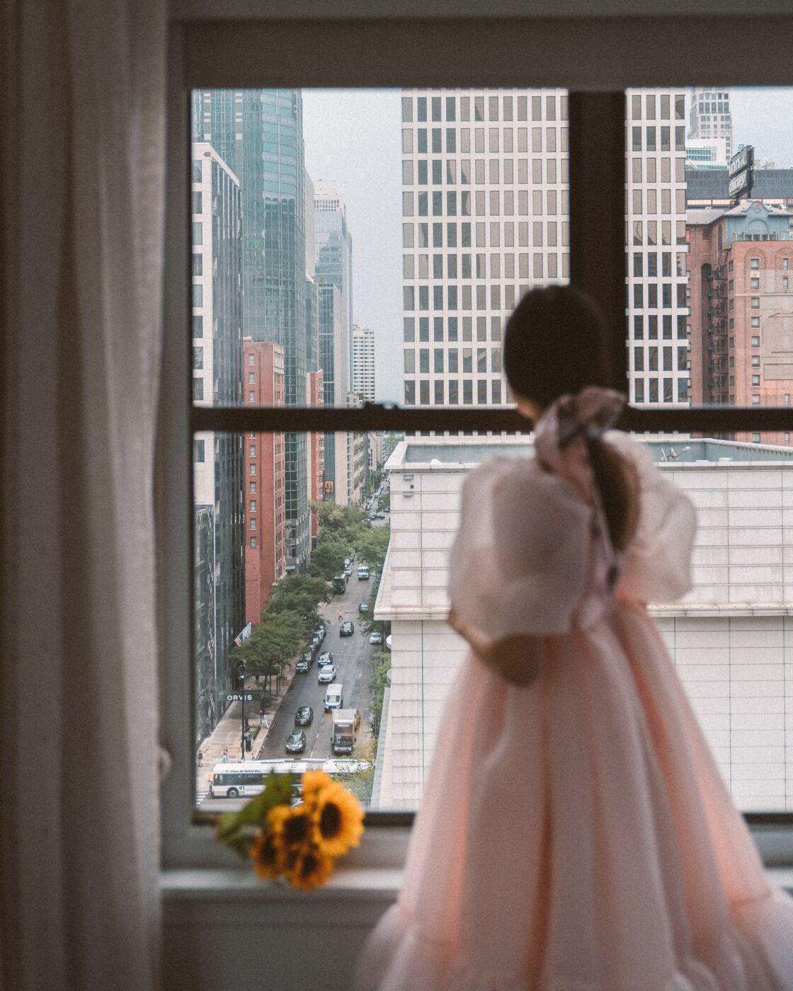 Girl in pink dress looking out hotel window in Chicago